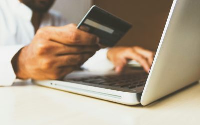 Person holding a credit card while entering payment details on a laptop during an online purchase.