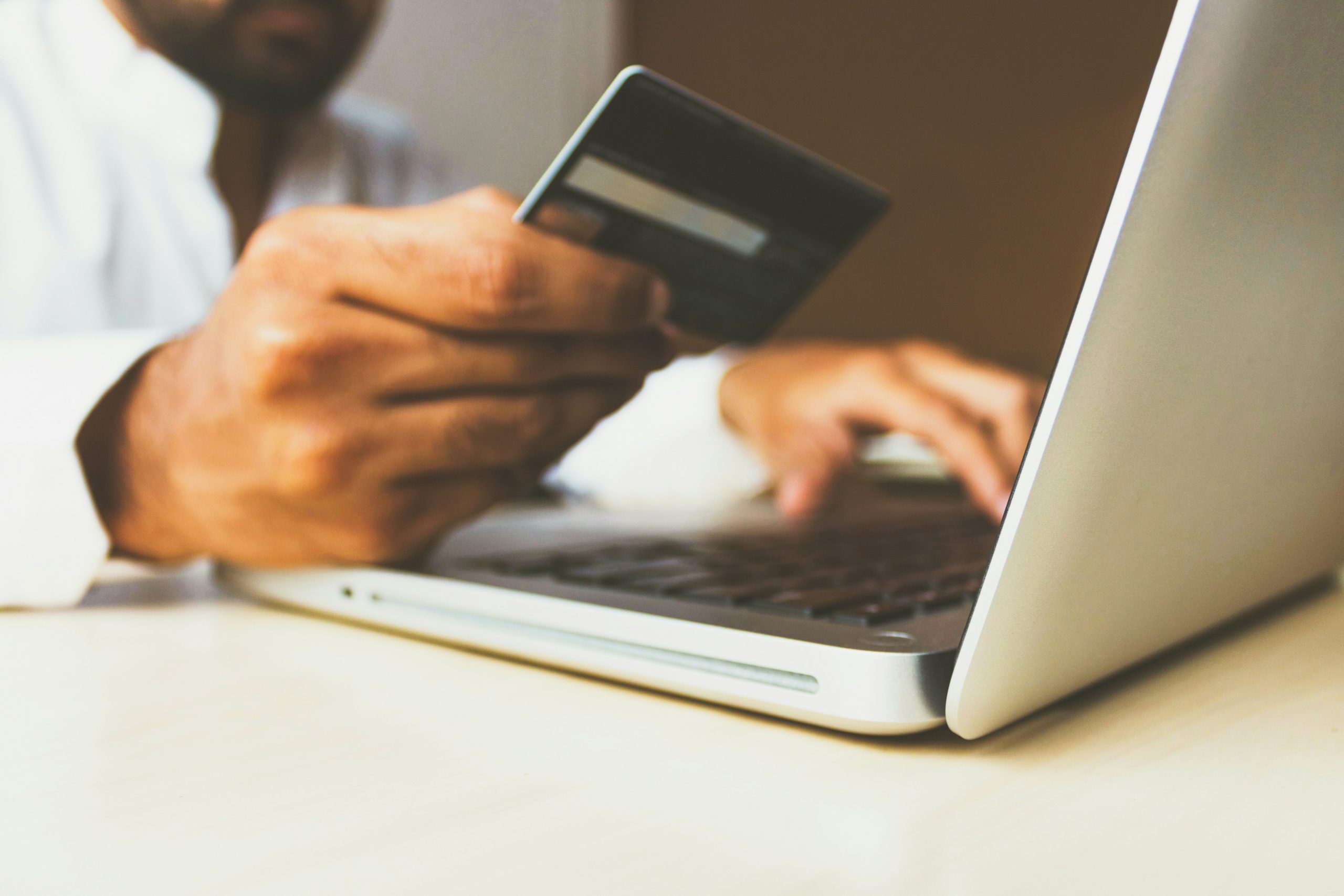 Person holding a credit card while entering payment details on a laptop during an online purchase.