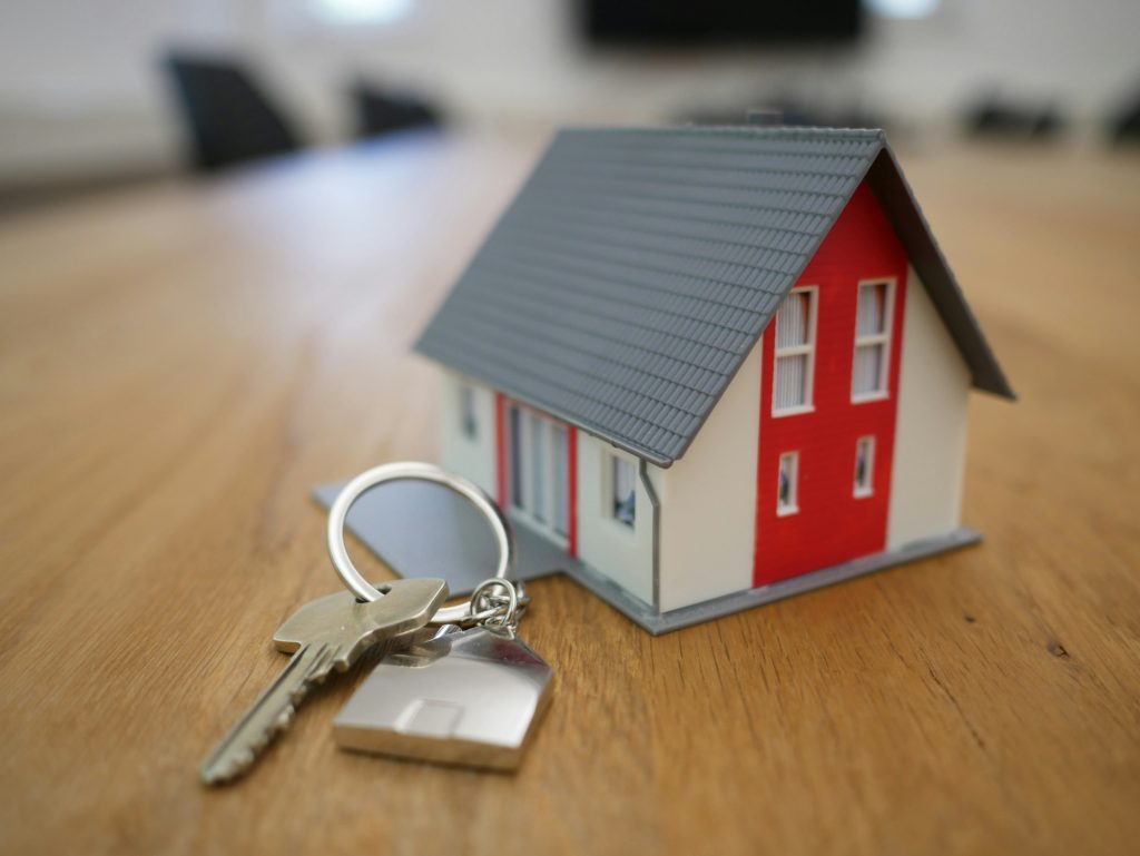 House keys beside a small model home on a wooden table.