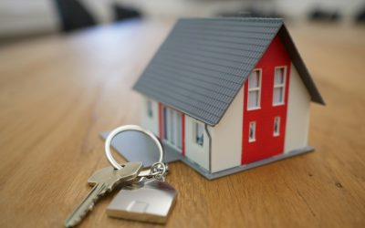 House keys beside a small model home on a wooden table.