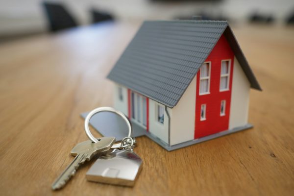 House keys beside a small model home on a wooden table.